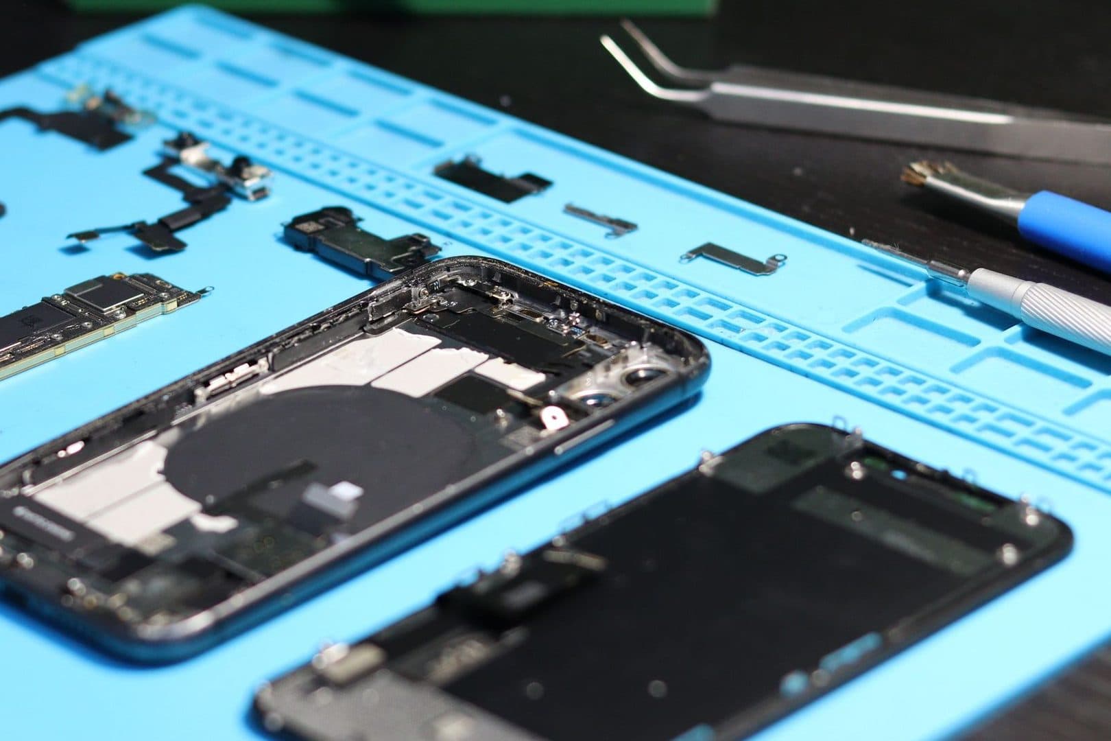 Zwei geöffnete Smartphones mit ausgebautem Logicboard und Kleinteilen auf einer blauen ESD-Matte